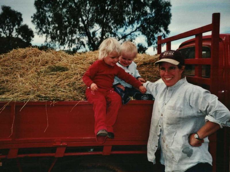 Rikke Nesbit i arbejdstøjet står ved en lastbil fyldt med halm. I halmen sidder 2 yngre børn.